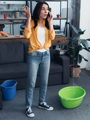 Full length view of shocked woman talking on phone while water leaking from ceiling